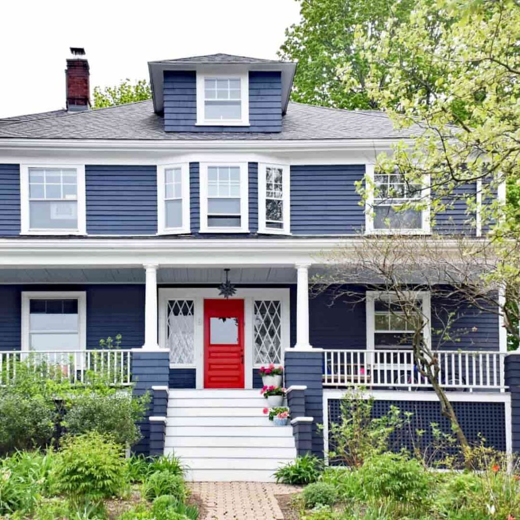 An image of Dark blue house with a bold red front door creating a striking entrance.
